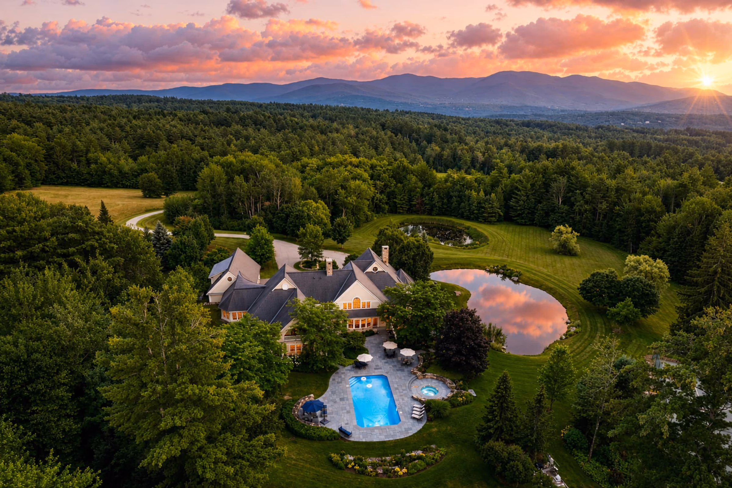 Breathtaking high-altitude sunset aerial view of the entire luxury estate, showing the main residence, swimming pool, and spring-fed pond.